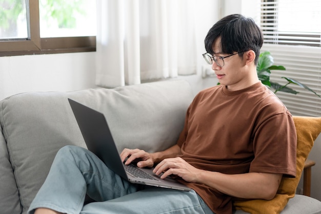 Technology Concept The man that is putting on glasses leaning his back on the dark yellow while focusing on the laptop’s screen.