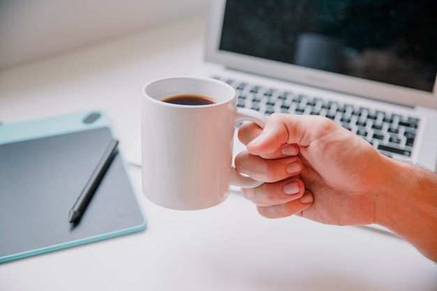 Technology and desk concept with hand holding mug