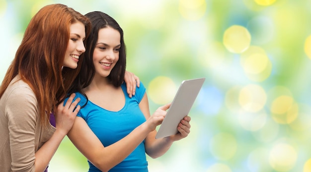 technology, friendship and people concept - two smiling teenage girls or young women pointing finger at tablet pc computer screen over green lights background