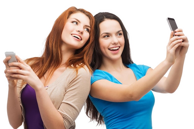 technology, friendship and people concept - two smiling teenagers taking picture with smartphone camera