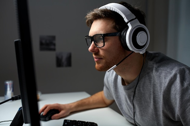 technology, gaming, entertainment, let&amp;#39;s play and people concept - young man in headset and glasses with pc computer playing game at home and streaming playthrough or walkthrough video