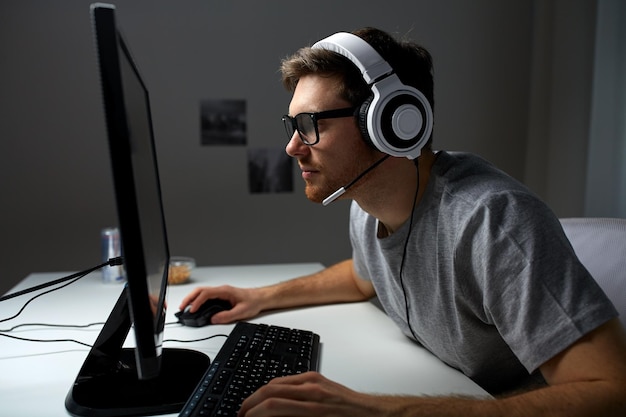 technology, gaming, entertainment, let&amp;#39;s play and people concept - young man in headset and glasses with pc computer playing game at home and streaming playthrough or walkthrough video