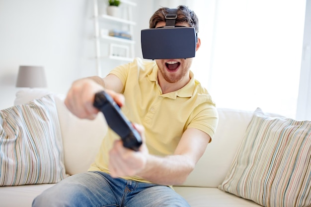 technology, gaming, entertainment and people concept - happy young man with virtual reality headset or 3d glasses with controller gamepad playing racing video game at home