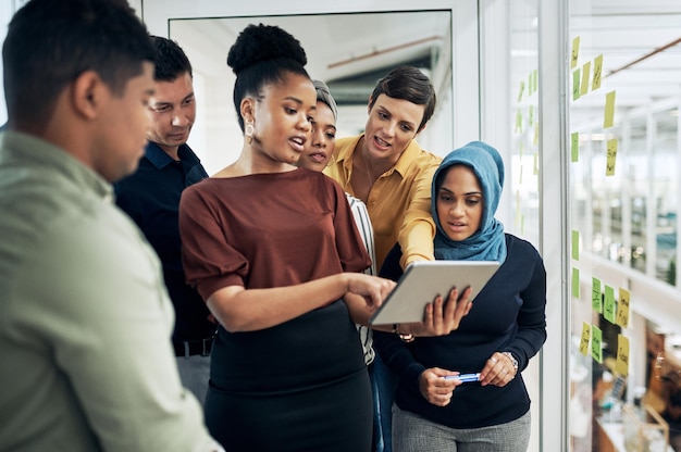 Technology helps them better understand their big plans Shot of a group of businesspeople using a digital tablet while brainstorming with notes on a glass wall in an office