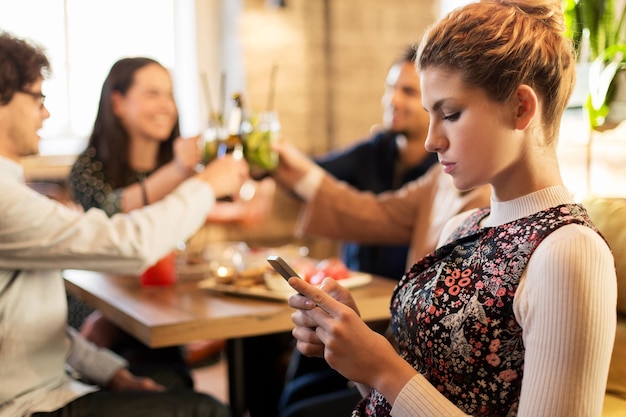 technology, lifestyle, holidays and people concept - woman with smartphone and friends at restaurant