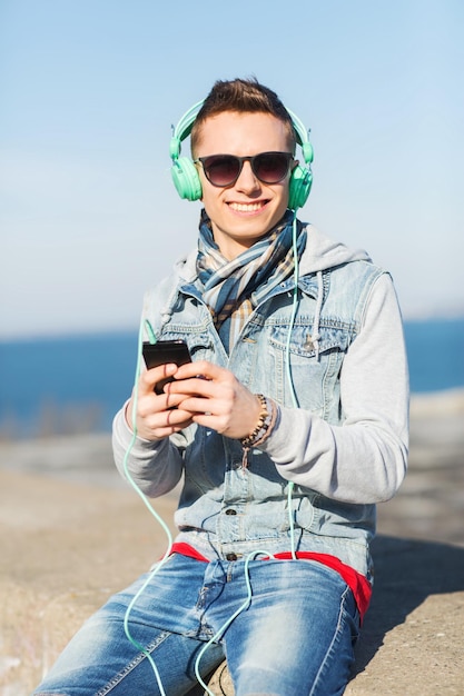 technology, lifestyle and people concept - smiling young man or teenage boy in headphones with smartphone listening to music outdoors