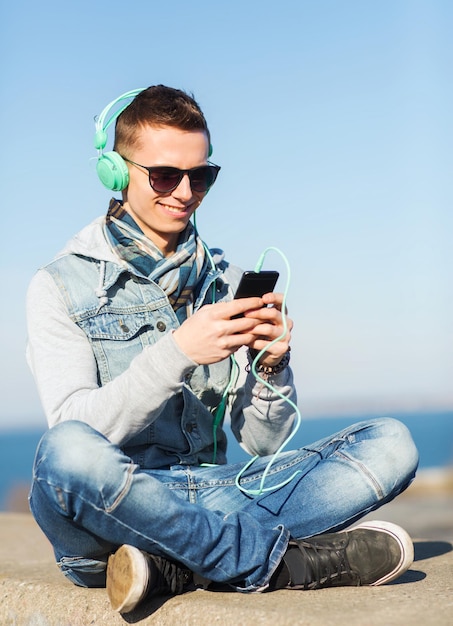 technology, lifestyle and people concept - smiling young man or teenage boy in headphones with smartphone listening to music outdoors