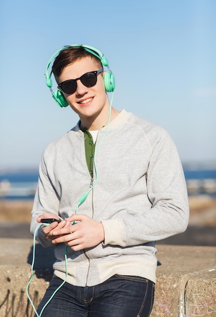 technology, lifestyle and people concept - smiling young man or teenage boy in headphones with smartphone listening to music outdoors