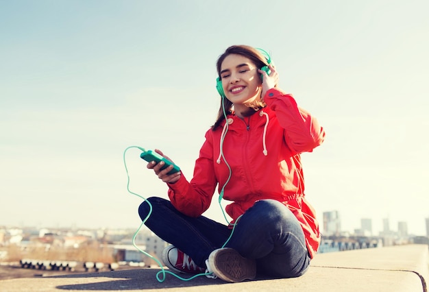 technology, lifestyle and people concept - smiling young woman or teenage girl with smartphone and headphones listening to music outdoors