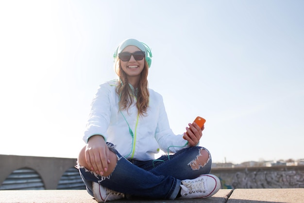 technology, lifestyle and people concept - smiling young woman or teenage girl with smartphone and headphones listening to music outdoors