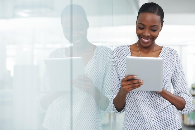 Technology makes work a pleasure Shot of a young woman leaning against a glass divider while using a digital tablet