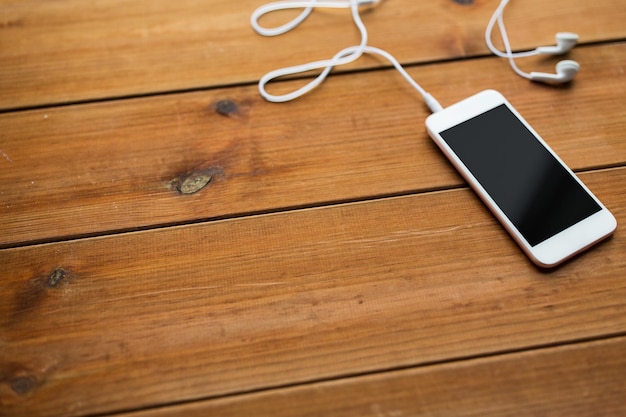 technology, music, gadget and object concept - close up of white smartphone and earphones on wooden surface with copy space