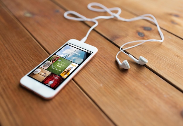 technology, music, gadget and object concept - close up of white smartphone and earphones on wooden surface with web applications on screen