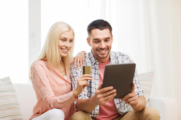 technology, people, e-money and commerce concept - smiling happy couple with tablet pc computer and credit or bank card shopping online at home