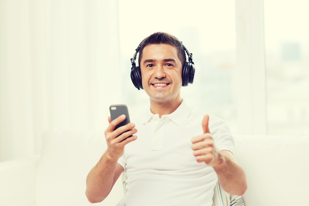 technology, people, lifestyle and distance learning concept - happy man with smartphone and headphones listening to music at home