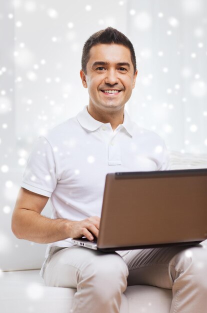 technology, people lifestyle and networking concept - happy man working with laptop computer at home over snow effect