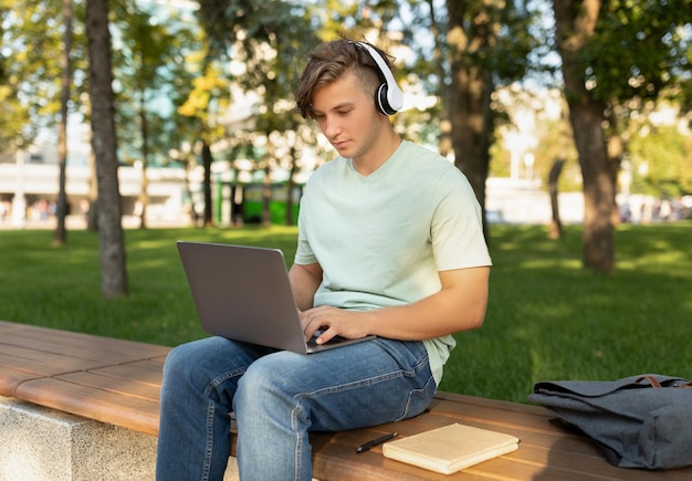 Technology and studentship concept male student using laptop computer and wearing headphones sitting