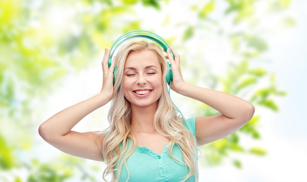 Photo technology, summer and people concept - happy young woman or teenage girl with headphones listening to music over green natural background