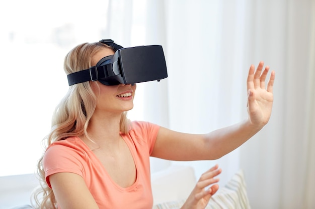 technology, virtual reality, entertainment and people concept - happy young woman with virtual reality headset or 3d glasses playing game at home and touching something invisible