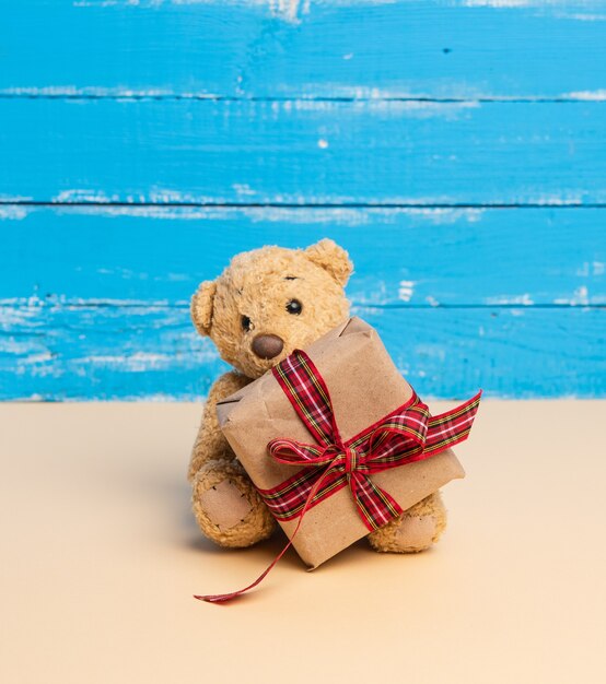 Photo teddy bear and blue square cardboard box with red bow on a blue wooden