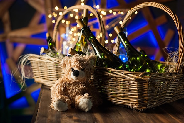 Teddy bear champagne bottle with Christmas basket gold garlands on dark brown wooden background new year celebration conceptxA