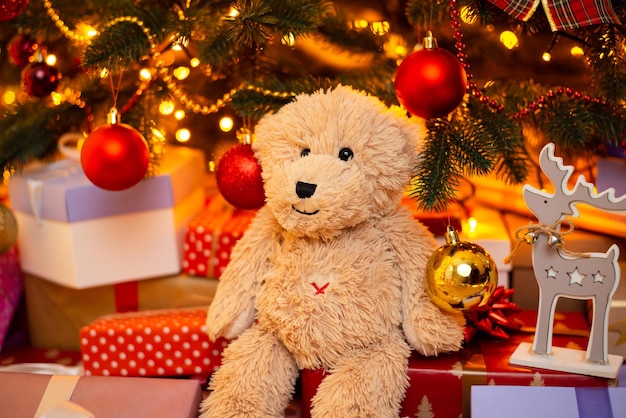 Teddy bear under decorated fir tree with many present boxes