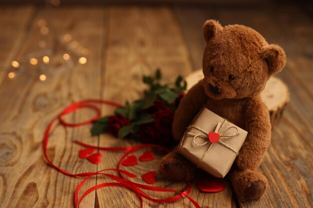 A teddy bear holds a gift in a craft box on a wooden background Picture for Valentines Day