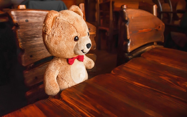 Teddy bear is sitting at the table. Wooden furniture and brown bear toy. A fairytale episode. The red butterfly.