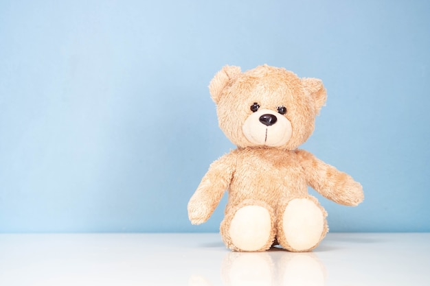 Teddy Bear sitting on a white table and blue wall.