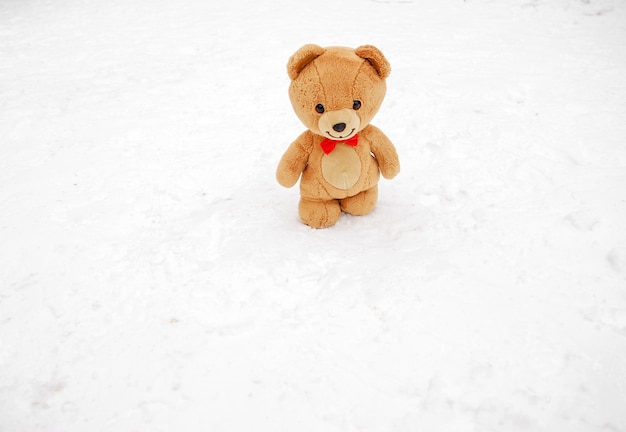 Teddy bear in winter. Winter concept. Brown teddy bear with a butterfly around its neck walks on a white snow, winter day. Toy outside