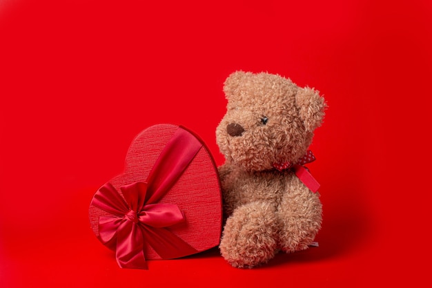 Photo teddy bear with heart shaped box isolated on red