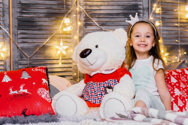 Teddy bear with little girl in a modern room with New Year's pillows and Christmas garlands