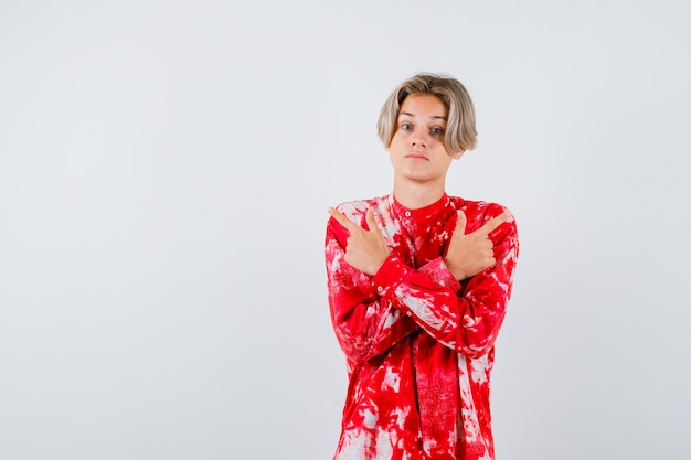 Teen blonde male pointing to opposite directions in oversized shirt and looking hesitant , front view.