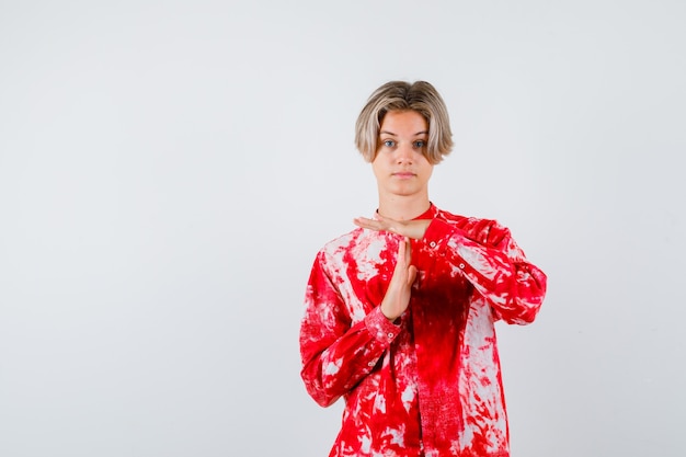 Teen blonde male showing time break gesture in oversized shirt and looking cheerless , front view.