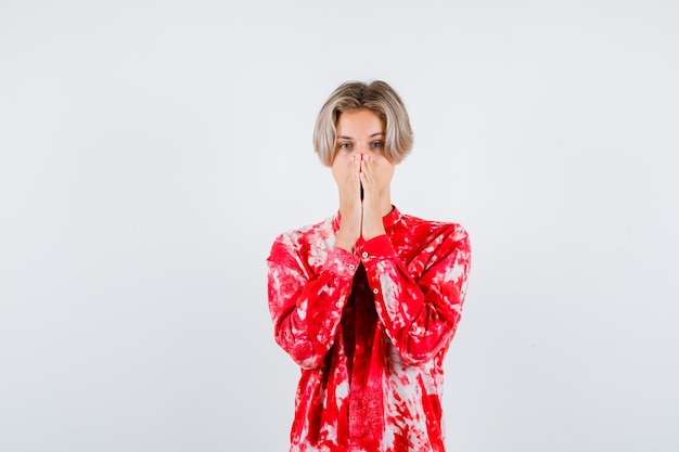 Teen blonde male with hands on face in oversize shirt and looking focused , front view.