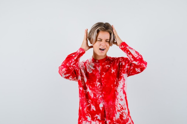 Teen blonde male with hands near head in oversized shirt and looking troubled. front view.