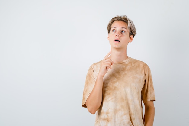 Teen boy keeping finger in the air, looking up in t-shirt and looking focused. front view.