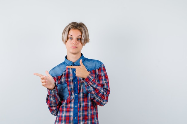 Teen boy pointing to the left side in checkered shirt and looking focused. front view.