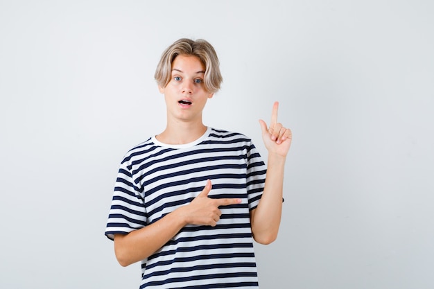 Teen boy pointing to the right side and up in t-shirt and looking astonished . front view.