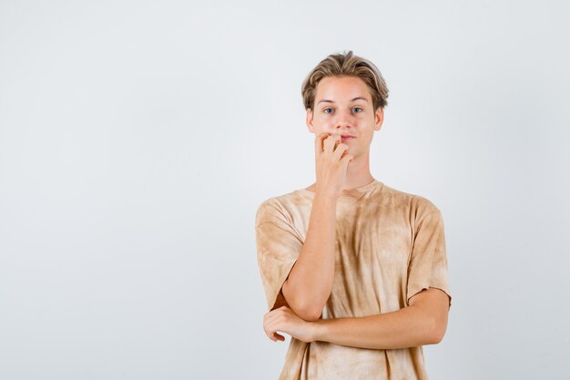 Teen boy standing in thinking pose in t-shirt and looking thoughtful , front view.