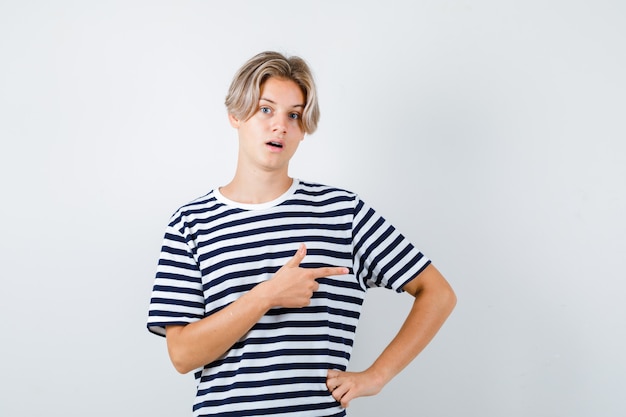 Teen boy in t-shirt pointing to the right side, opening mouth and looking shocked , front view.