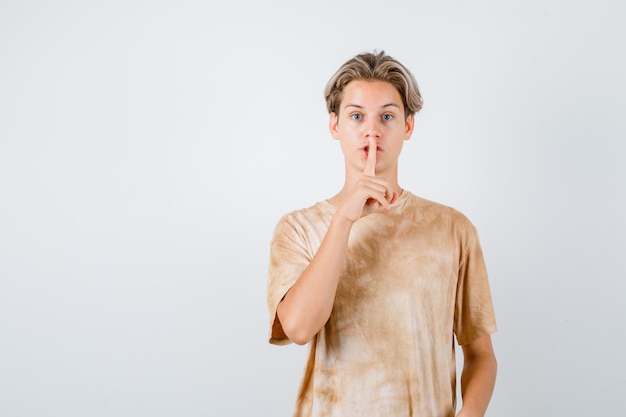 Teen boy in t-shirt showing silence gesture and looking careful , front view.