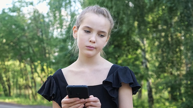 Teen girl in black dress looks at phone unsatisfied closeup