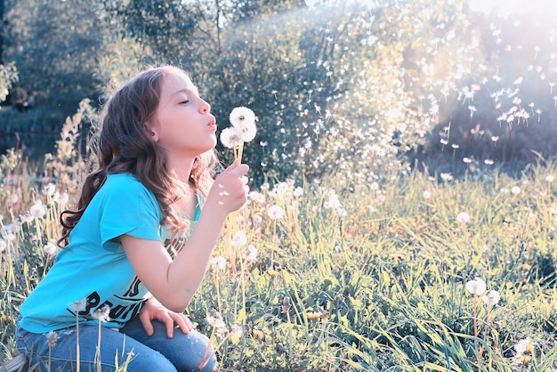 Photo teen girl blowing seeds from a flower dandelion in a spring park