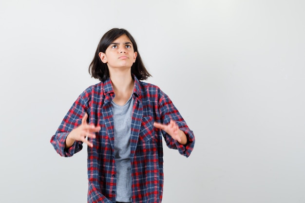 Teen girl in checkered shirt pretending to holds something and looking wistful , front view.