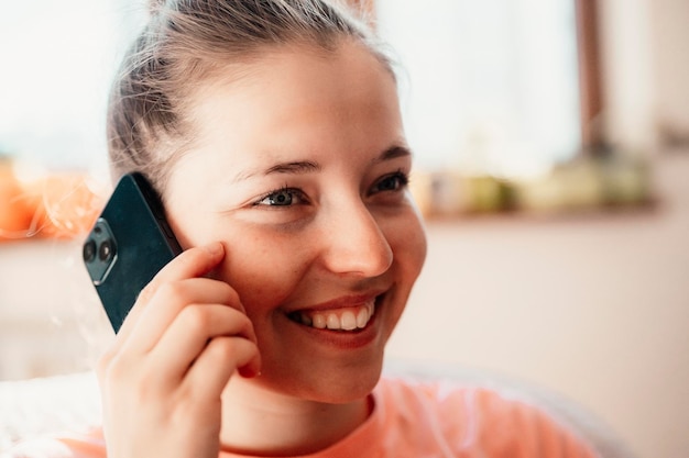 Teen girl checking social media holding smartphone at home Smiling young woman using mobile phone app playing game shopping online