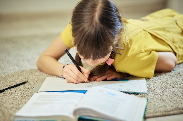 Teen girl doing homework sitting on the carpet in her room