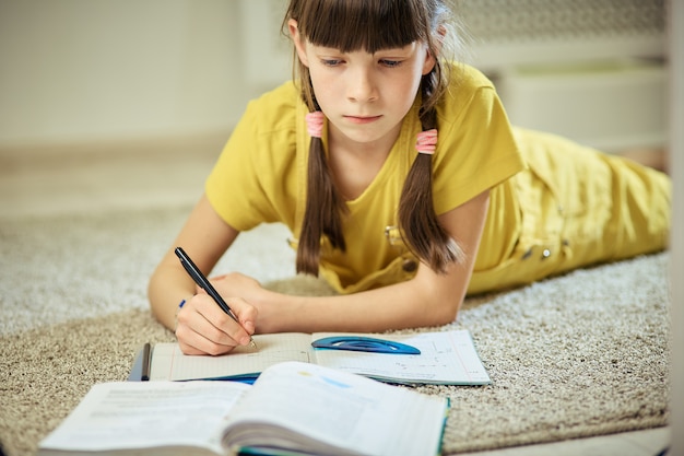 Teen girl doing homework sitting on the carpet in her room