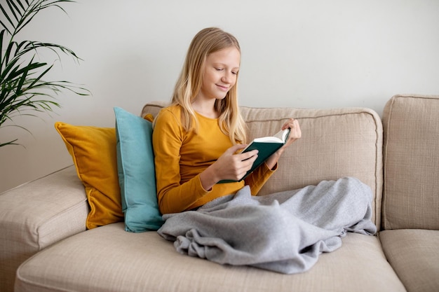 Teen girl enjoying a book on a cozy sofa in daylight