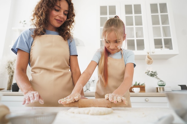 Teen girl helping her mom to cook dough in their kitchen at home